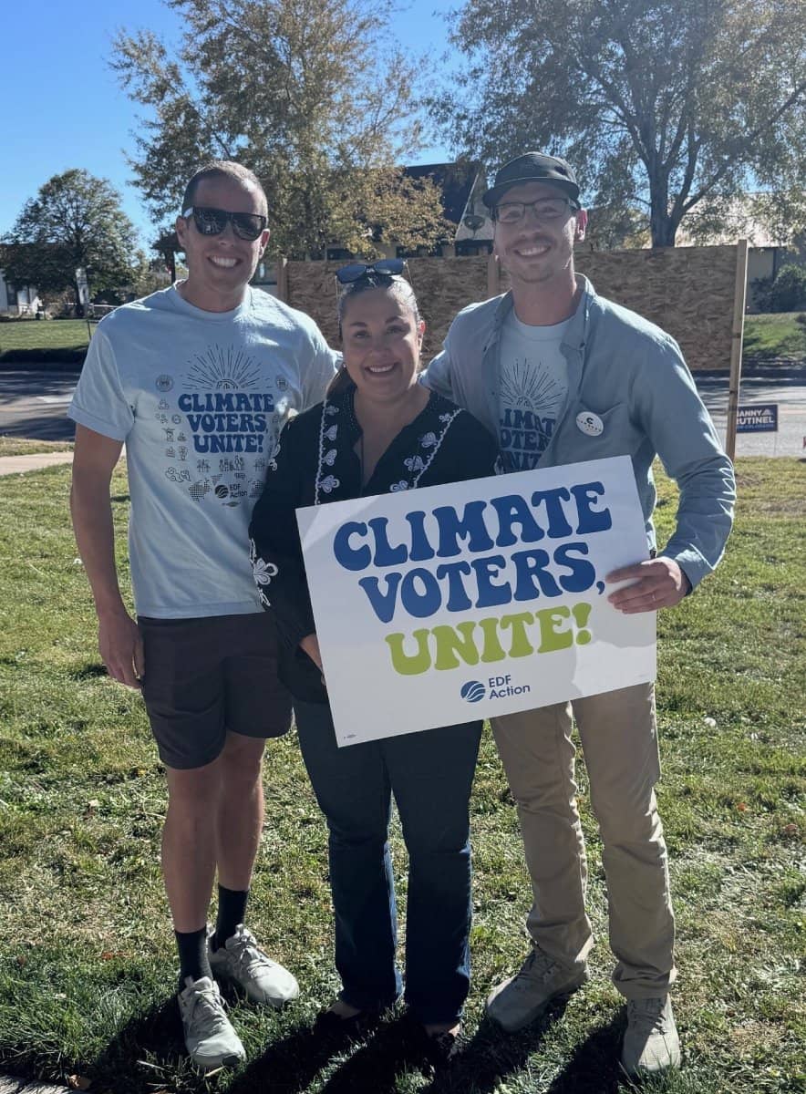 Three people standing together holding a "Climate Voters, Unite" sign